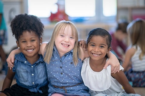 3 preteen girls in a playroom hug each other. 
