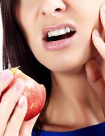 A woman eating an apple holds her jaw in pain. 