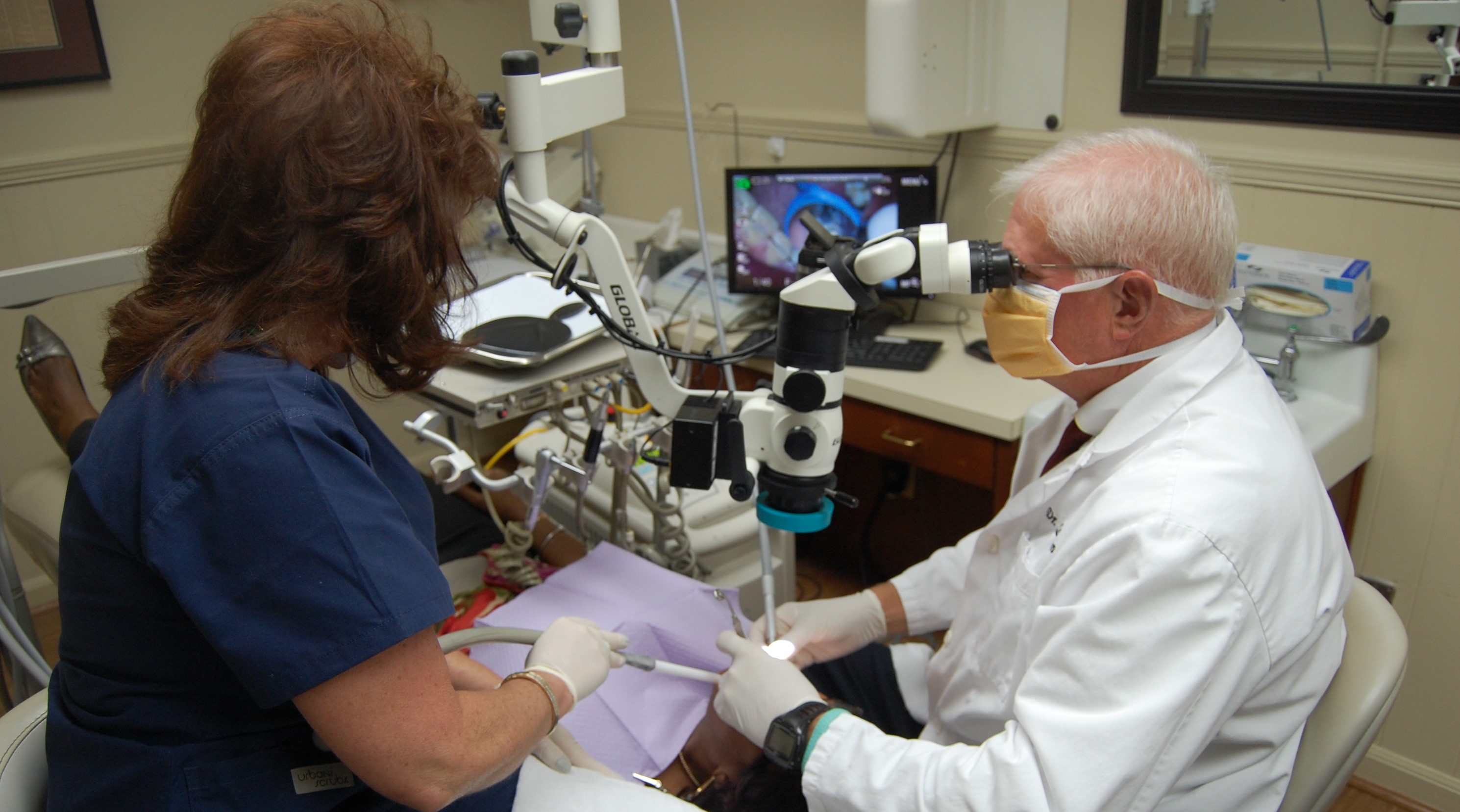 Dentist at microscope conducting research with assistant to his left