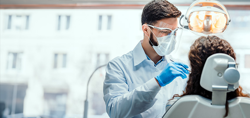 A dentist cleaning the teeth of a woman, who is sitting in a dentist's chair