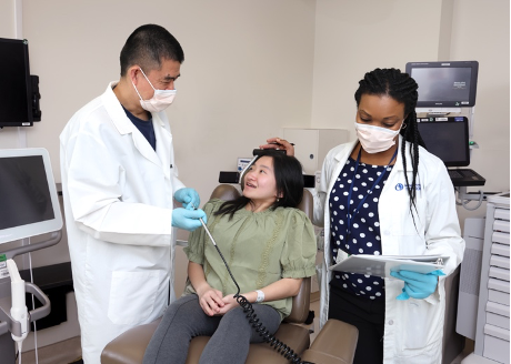 A patient is sitting in a dental chair while two dental professionals are examining them.