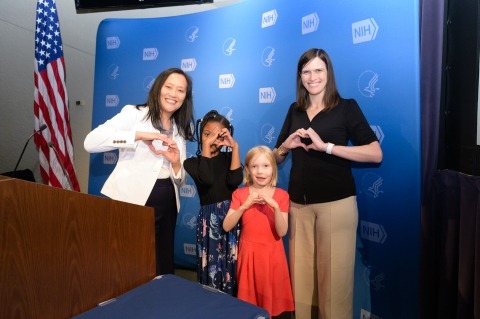 Two women and two girls smiling and making hearts with their hands