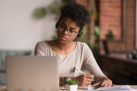 Young woman looking at a laptop and writing in a notebook
