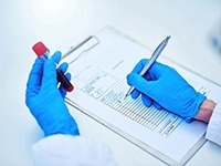 A person holding a tube of blood sample and making notes.