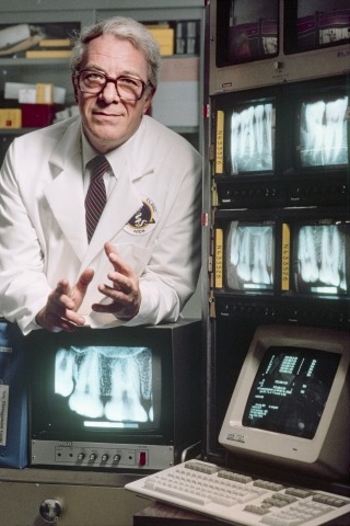 Harald Löe with multiple monitors displaying x-rays of teeth. 