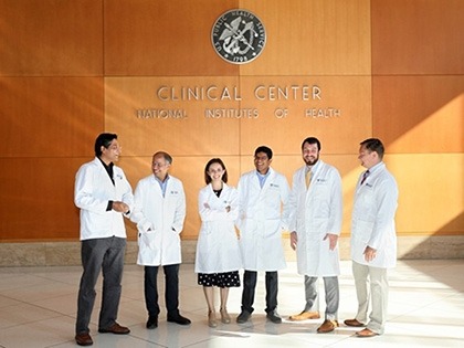 A group of people are standing in a horizontal line while conversing with each other in front of the NIH Clinical Center.