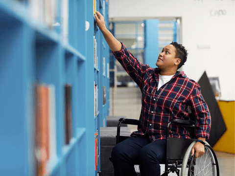  A person with disabilities using a wheelchair, searching through books on a shelf.