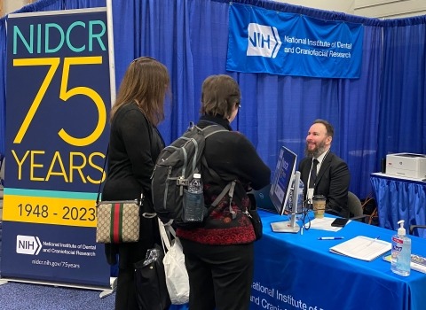 A group of people standing at a table with a sign that says NIDCR 75th anniversary.