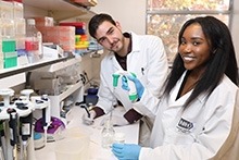 Two researchers working in the lab while smiling at the camera.