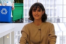 A woman sitting at a desk with a recycling bin nearby, promoting eco-friendly practices.