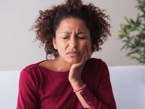 A woman in pain holding her face due to TMDs.