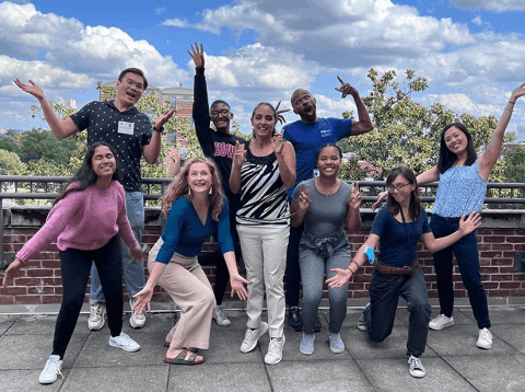 A group of nine people are standing together and making funny poses at the camera.