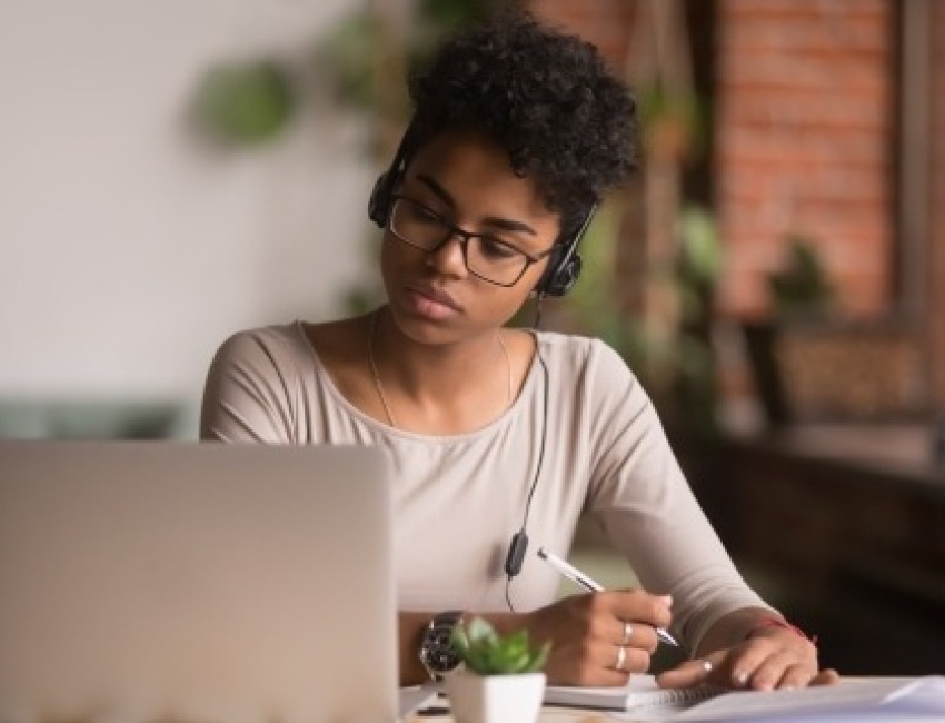 Young woman looking at a laptop and writing in a notebook
