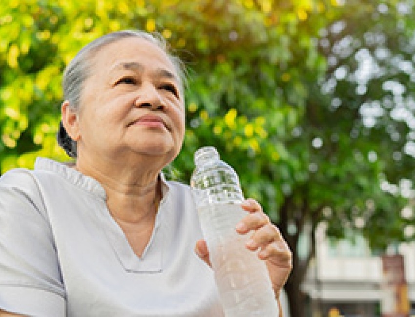 An older woman is sitting outdoors drinking water from a bottle.