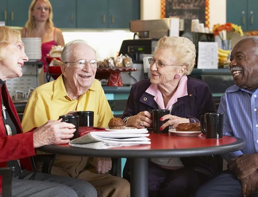 Amigos mayores alrededor de una mesa compartiendo en un café.