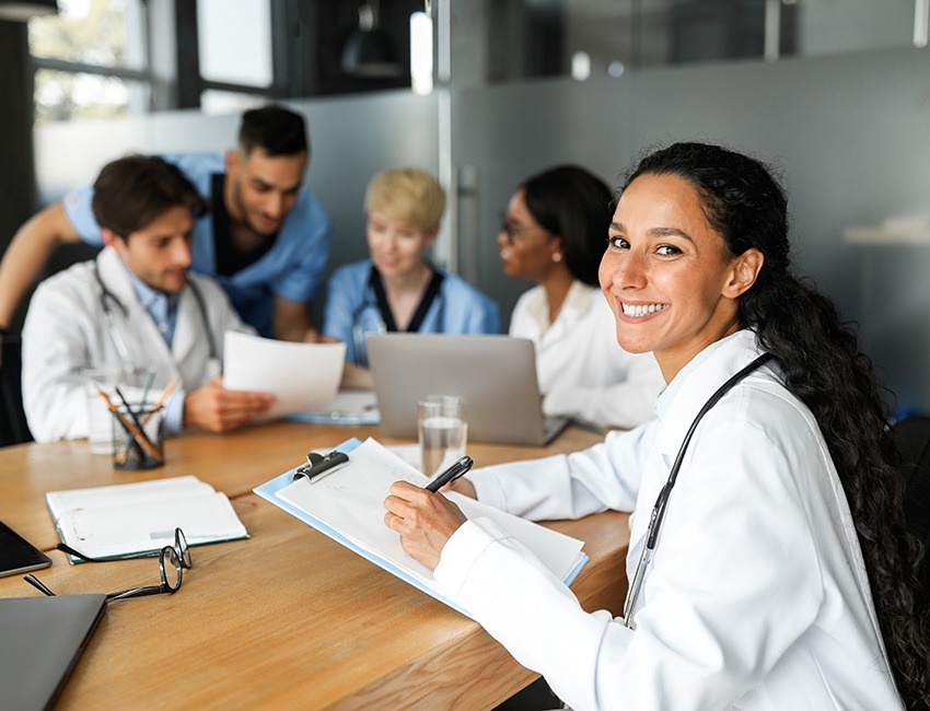 A female researcher sitting and smiling while holding a clipboard, with four researchers sitting behind her