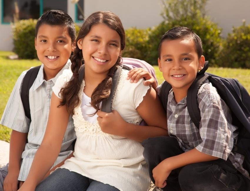 Dos niños y una niña con mochilas y sonriendo