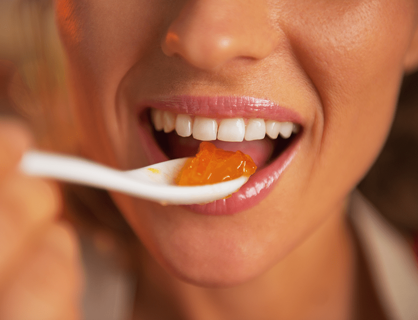 A woman eats a spoonful of jelly.