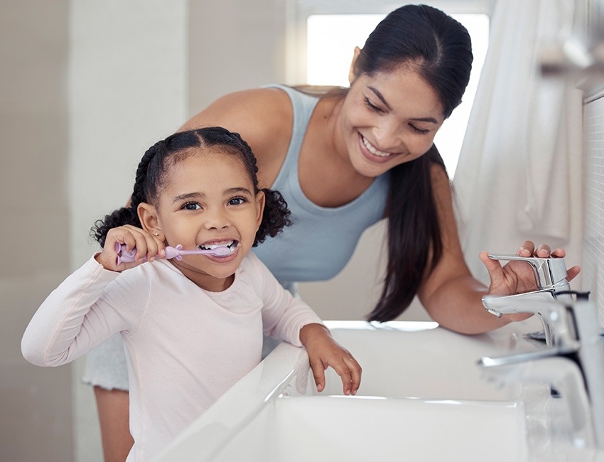 Niña se cepilla los dientes junto a su mamá. 