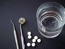 Stock image of opioids next to dental tools and a glass of water