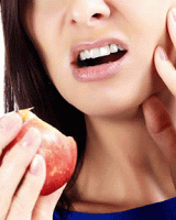 A woman holding her jaw after biting into an apple to depict a TMD (Temporomandibular Disorder). 